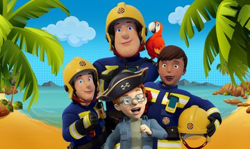 Fireman Sam in his navy blue uniform and yellow helmet crosses his arms while a parrot sits on his shoulder. In front of him are two other firefighters and a small red haired boy in a blue jacket, glasses and a pirate hat. They all stand on a beach.