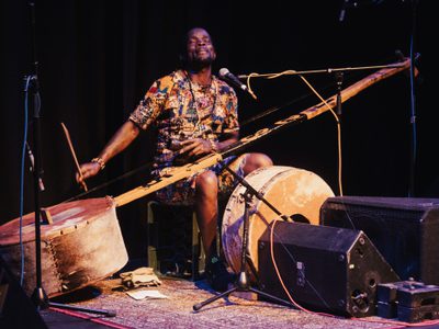 Gasper Nali sat on stage with his babatoni laid across his lap and kick drum in front of him. He has his eyes closed as he plays and has a microphone in front of him