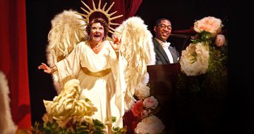 Wendi Peters dressed as an angel playing the part of Florence Foster Jenkins. Next to her is Matthew James Morrison at the piano