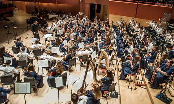 An orchestra of young musicians all in blue dress, or white shirts with blue ties, performing on The Anvil stage