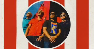 The four members of Haircut One Hundred are stood together dressed for summer. The image of them is a circle and around the circle are red and white vertical stripes.