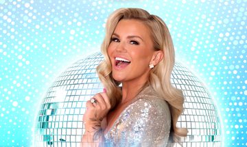 Kerry Katona in a silver sequin top, stood facing left with her head turned to the camera smiling with a large disco ball behind on a blue sparkly background