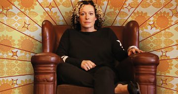 Kate Rusby in a large leather chair with 60s style wallpaper behind her