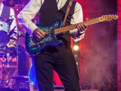 A man in a bowler hat playing guitar on stage