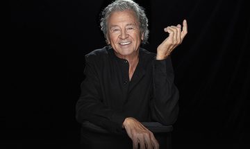 Ian Gillan wearing a black shirt and smiling in front of a black background.