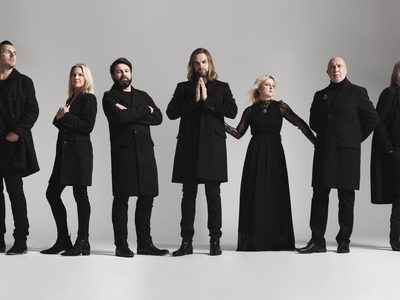 5 men and two women wearing all-black clothes, doing various poses across a grey background.