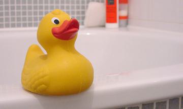 A yellow rubber duck sits on the side of a bath tub