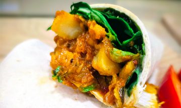 A curry filled wrap. The wrap contains curried rice, chickpeas, and potatoes, with spinach