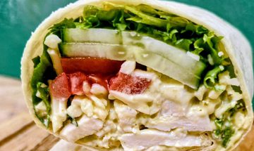 A tortilla wrap filled with chicken, pesto, grated cheese, tomato, and salad