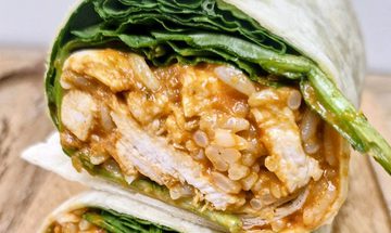 A tortilla wrap filled with chicken, salad, tikka sauce, and mango chutney