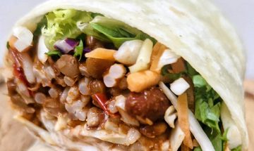A tortilla wrap filled with salad, cheese, beans, and sauce