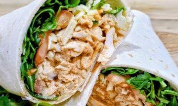A Cajun chicken wrap on a wooden board. The wrap has chopped seasoned chicken in a thin marinade with lettuce and tomatoes