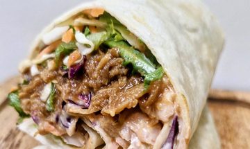 A tortilla wrap filled with pulled pork, coleslaw, and salad