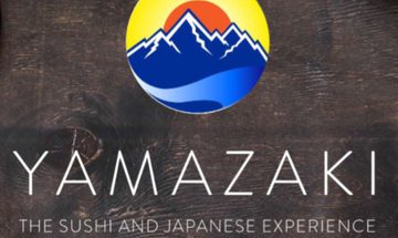 A logo with blue mountains with a red sun and yellow sky behind on a black wooden background with the words 'Yamazaki The Sushi and Japanese Experience'